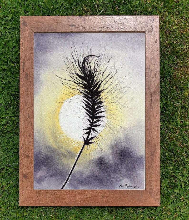 The grass seed head silhouette painting in a wooden frame laid on a lawn.