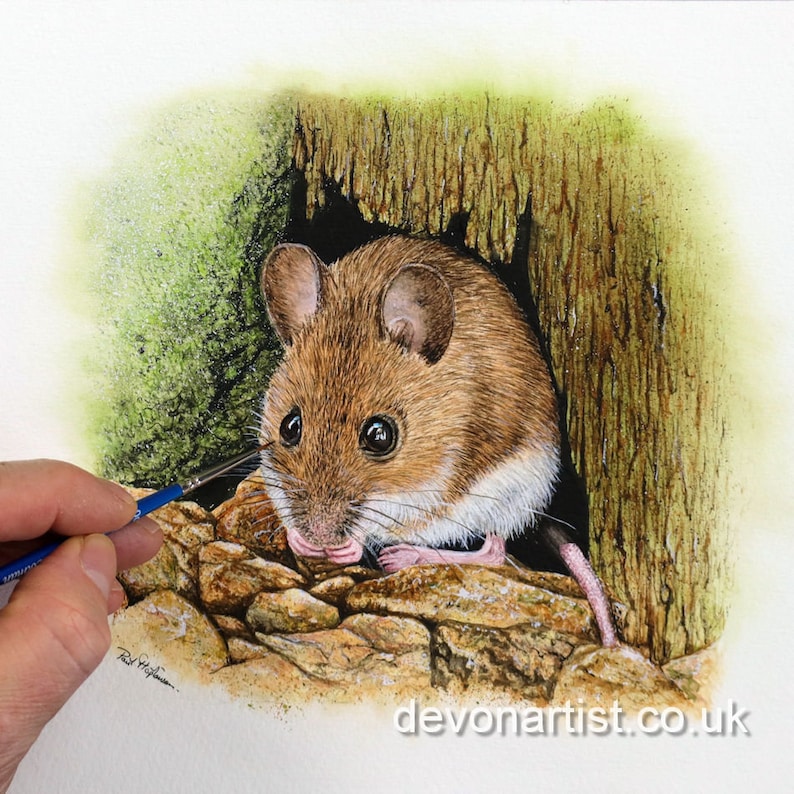Paul finishing off painting a wood mouse.  The animal is in a hole at the base of some broken wood, with little bits of gravel at its feet.  The mouse as large, black shiny eyes and large round ears too.  It has been painted in an illustrative style.