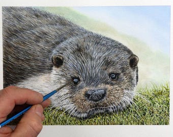 May include: A close-up of a watercolour painting of an otter. The otter is lying on its belly with its head turned to the side. The otter's fur is a mix of brown and grey, and its eyes are dark brown. The otter's nose is black, and its whiskers are white.