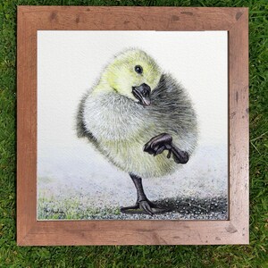The gosling painting in a square wood frame which is laid on a lawn.