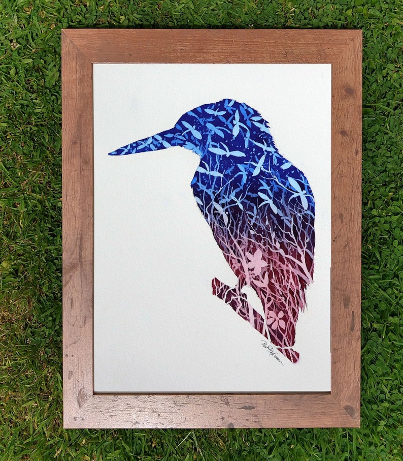 The finished kingfisher painting in a wooden frame which has been laid on a lawn.