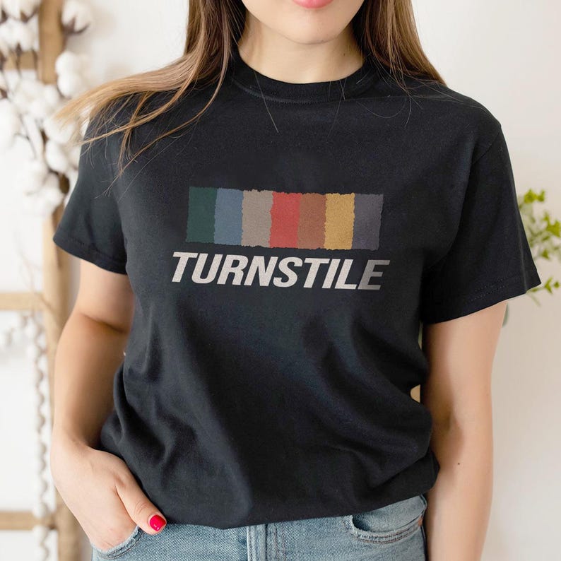 May include: Black t-shirt featuring the word "TURNSTILE" in white, with a rectangular color block design above the text. The color block includes shades of green, blue, gray, red, yellow, and brown.