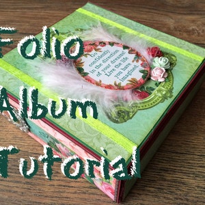 May include: A green and pink scrapbook album with a white feather and a floral embellishment. The album has a quote on the front that reads "Go confidently in the direction of your dreams! Live the life you have imagined."