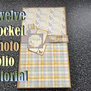 Op de afbeelding: Een handgemaakt fotoalbum met een bloemen- en ruitpatroon. De omslag bevat de tekst "Twelve Pocket Photo Folio tutorial". Het album is versierd met decoratieve labels en een metalen clip, perfect voor het bewaren van foto's en souvenirs.
