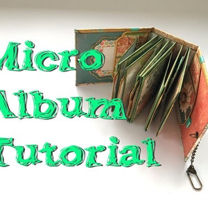 May include: A small, multi-colored, fabric-covered album with a chain attached. The album is open to reveal several pages with decorative paper. The text "Micro Album Tutorial" is written in green letters on a white background.