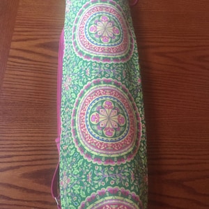 May include: A green and pink yoga mat carrier with a floral pattern. The carrier has a drawstring closure and a zipper.
