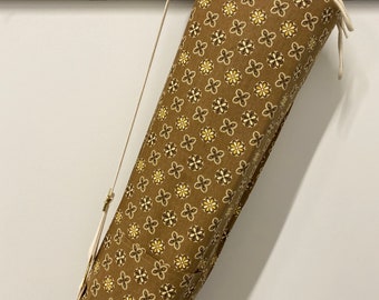 May include: A brown yoga mat bag with a white strap and drawstring closure. The bag has a floral pattern in shades of brown and yellow.