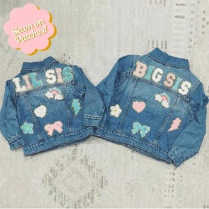 Può includere: Due giacche di jeans con toppe colorate cucite sul retro. Una giacca dice "Lil Sis" e l'altra dice "Big Sis".