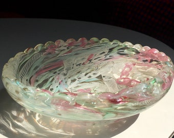 Puede incluir: Un cuenco de vidrio transparente con un borde festoneado. El cuenco está decorado con remolinos de vidrio rosa, verde y blanco.