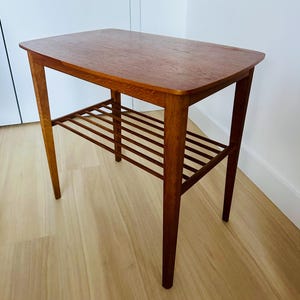 May include: A rectangular wooden side table with a lower slatted shelf. The table has a warm brown finish and tapered legs. The tabletop is approximately 24 inches long and 16 inches wide.