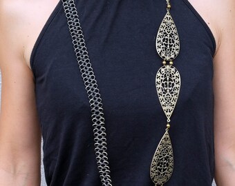 May include: A silver chain necklace with a long, dangling pendant made of gold metal. The pendant is a series of three teardrop-shaped pieces with intricate cut-out designs.