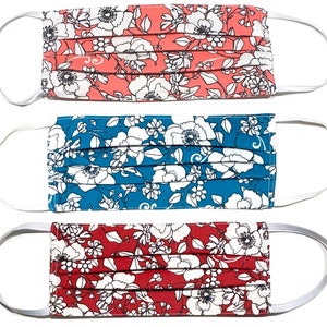 May include: Three fabric face masks with white floral patterns on a red, blue, and pink background. The masks have white elastic ear loops.