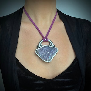 May include: A silver pendant necklace with a large amethyst crystal set in a silver frame. The necklace is on a purple cord.