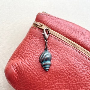May include: A red leather zipped pouch with a metal seashell charm attached to the zipper pull.