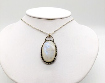 May include: A silver chain necklace with a silver and gold oval pendant featuring a white moonstone.