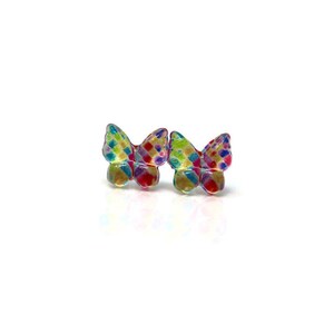 May include: A pair of colorful butterfly-shaped stud earrings. The earrings feature a mosaic pattern of red, blue, green, and yellow. The wings are slightly translucent, and the studs are set against a white background.