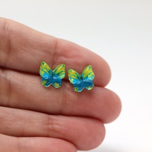 May include: A pair of butterfly-shaped stud earrings. Each earring features a vibrant design with yellow and blue marbling. The earrings are small, delicate, and likely made of resin or a similar material. The butterfly wings are detailed.