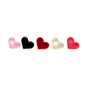 Könnte beinhalten: Fünf herzförmige Objekte in einer Reihe, jedes in einer anderen Farbe. Die Farben sind Rosa, Schwarz, Rot, Off-White und Magenta. Die Herzen sind glatt und glänzend, mit einer abgerundeten Form.