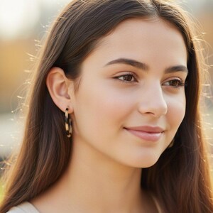 May include: A woman wearing tortoiseshell hoop earrings. The earrings are a circular design with a pattern of brown and tan colors. The woman has long brown hair and is smiling.