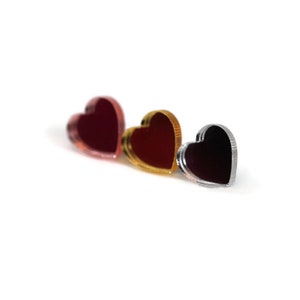 May include: Three heart-shaped decorative items in a row. The hearts are in shades of red, gold, and silver. The items are reflective and appear to be made of a shiny material, possibly acrylic or metal.