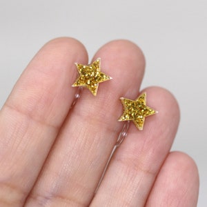Pu&ograve; includere: Un paio di orecchini a stella con glitter dorati. Gli orecchini a forma di stella hanno un retro trasparente e sono riempiti di glitter dorati. Gli orecchini sono piccoli e delicati, perfetti per aggiungere un tocco di brillantezza.