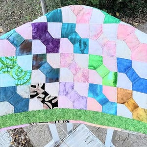 Op de afbeelding: Een patchworkdeken met een groene rand en een patroon van vierkanten en ruiten in verschillende tinten roze, blauw, paars en groen.