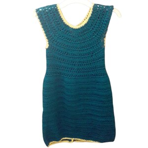 May include: Teal crochet dress with a scoop neckline and cap sleeves, hanging on a white hanger. The dress has a fitted bodice and a slightly flared skirt. The neckline and sleeve edges are trimmed with a light yellow yarn.