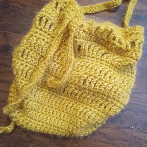 Peut inclure: Sac au crochet jaune moutarde avec fermeture à cordon et bandoulière. Le sac fait main présente un motif de point texturé et un bord festonné. Le sac est fait d'un matériau en fil doux et convient au transport de petits objets.