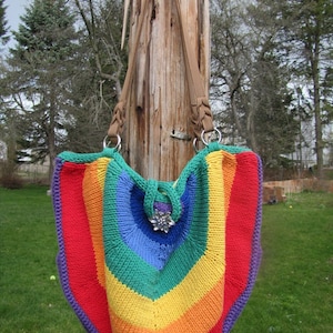 May include: A rainbow crocheted tote bag with a purple and silver embellishment hanging from a wooden post.