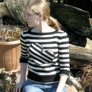 May include: A black and white striped sweater with a black and white striped heart on the front. The sweater has a crew neck and long sleeves.