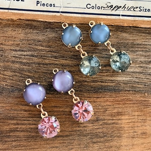 May include: Three pairs of vintage earrings with a gold-tone metal setting. Each earring has a large, round, light-coloured stone at the top and a smaller, faceted stone at the bottom. The top stones are blue and purple, and the bottom stones are blue and pink.
