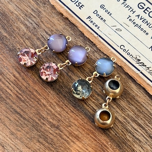 May include: Close-up of several pairs of vintage earrings with gold-tone metal settings. The earrings feature a variety of colourful gemstones, including pink, purple, blue, and clear stones. The earrings are displayed on a wooden surface.