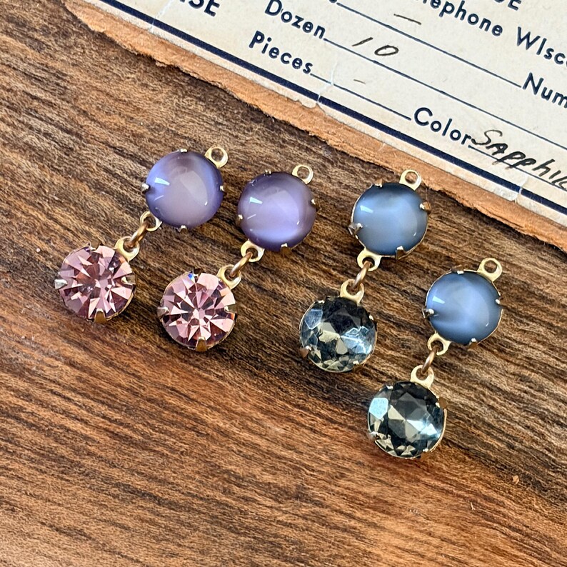 May include: Four pairs of dangling earrings with gold-coloured metal findings. Each earring features a round, faceted gemstone at the bottom and a round, cabochon-cut stone at the top. The gemstones are in shades of pink, purple, and blue.