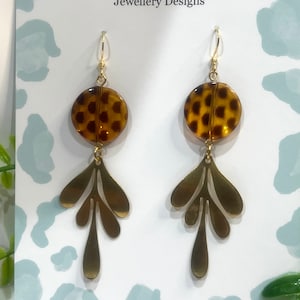 May include: Gold dangle earrings with a brown and black leopard print circle charm and a gold leaf design. The earrings are on a white card with the text "Curvy Leopard Jewellery Designs" and "Handmade Jewellery by Shaz".