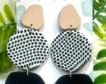 May include: A pair of black, white, and beige dangle earrings with a polka dot pattern. The earrings are made of polymer clay and have a gold hook.