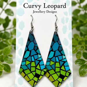 May include: A pair of diamond-shaped drop earrings featuring a mosaic pattern of blue, teal, and lime green geometric shapes. The earrings are displayed on a white card labelled Curvy Leopard Jewellery Designs and Handmade Jewellery by Shaz.