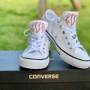 Puede incluir: Un par de zapatillas Converse de cuero blanco con las iniciales bordadas en rosa "LFF" en el lateral. Las zapatillas est&aacute;n en una caja blanca con la palabra "CONVERSE" impresa en la parte superior.