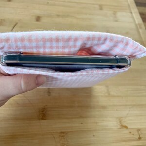 Op de afbeelding: Een roze en witte gingham stoffen tasje met een zwart rechthoekig voorwerp erin.