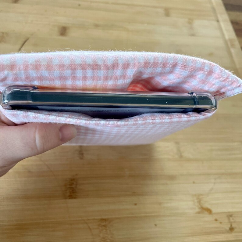 Op de afbeelding: Een roze en witte gingham stoffen tasje met een zwart rechthoekig voorwerp erin.