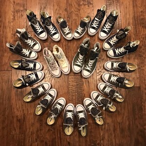 Puede incluir: Una colecci&oacute;n de 18 zapatillas de lona altas de color verde y negro dispuestas en forma de coraz&oacute;n sobre un suelo de madera. Las zapatillas tienen varios dise&ntilde;os y patrones, incluyendo algunas con la palabra "Converse" impresa en el lateral.