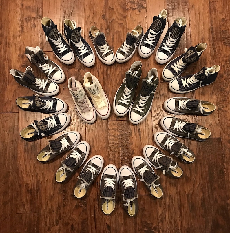Puede incluir: Una colecci&oacute;n de 18 zapatillas de lona altas de color verde y negro dispuestas en forma de coraz&oacute;n sobre un suelo de madera. Las zapatillas tienen varios dise&ntilde;os y patrones, incluyendo algunas con la palabra "Converse" impresa en el lateral.