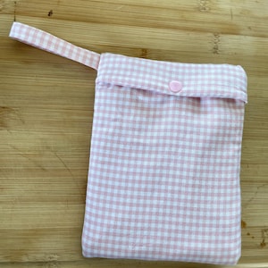 Op de afbeelding: Een herbruikbare tas van roze en wit gingham stof met een roze knoopsluiting en een roze stoffen handvat.