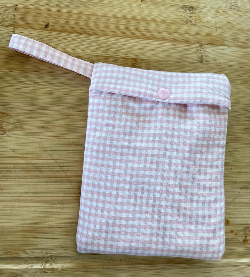 Op de afbeelding: Een herbruikbare tas van roze en wit gingham stof met een roze knoopsluiting en een roze stoffen handvat.
