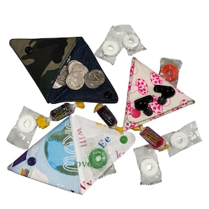 Könnte beinhalten: Eine Sammlung handgefertigter dreieckiger Stoffbeutel mit verschiedenen Mustern, darunter Camouflage, Denim und ein Pilz-Design. Jeder Beutel hat einen Druckknopfverschluss und enthält Münzen, Ohrhörer und Süßigkeiten.