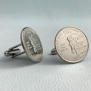 May include: A pair of silver cufflinks featuring the New Hampshire state quarter. The front of the cufflinks features the Old Man of the Mountain, a rock formation that was a popular tourist attraction in New Hampshire. The back of the cufflinks features the state motto, "Live Free or Die".