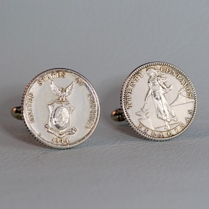 May include: A pair of silver cufflinks featuring a silver coin with the text "UNITED STATES OF AMERICA 1944" and a silver coin with the text "TWENTY CENTAVOS PHILIPPINES".