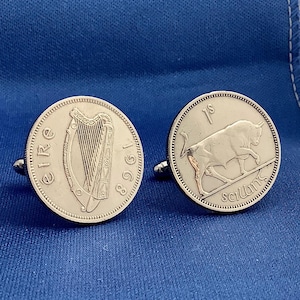 May include: Silver cufflinks featuring Irish coins. One cufflink displays a harp and the word "Eire" with the year 1968. The other cufflink shows a bull and the word "scilling". The cufflinks are set against a blue background.