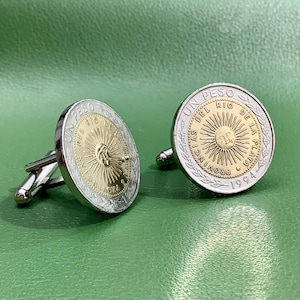 May include: Silver cufflinks with a gold-toned coin design featuring the text "UN PESO DEL RIO DE LA PLATA PROVINCIA 1994".