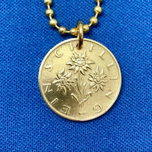 May include: A gold chain necklace with a gold coin pendant featuring three stylized edelweiss flowers and the inscription "SCHWEIZ 1969".