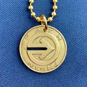 May include: Gold necklace with a round pendant featuring the words "PATH" and "NY-NJ" and a black arrow pointing to the right.